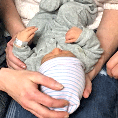 An image of a newborn baby being held by multiple hands