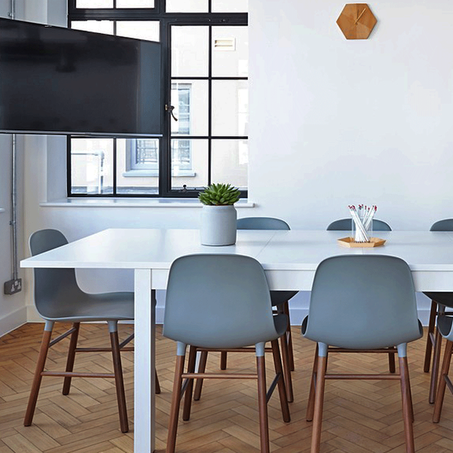 Image of a room containing a table and chairs, with a TV screen on the wall