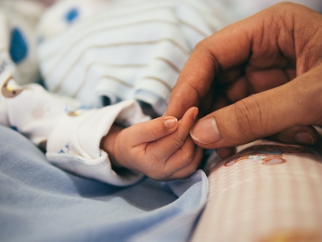 An adult hand holding an infant hand