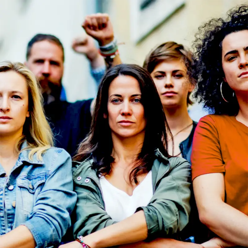 An image of five people. The three people in the front row are sitting with their arms crossed. The two people in the back row are standing, and one person has an arm raised.